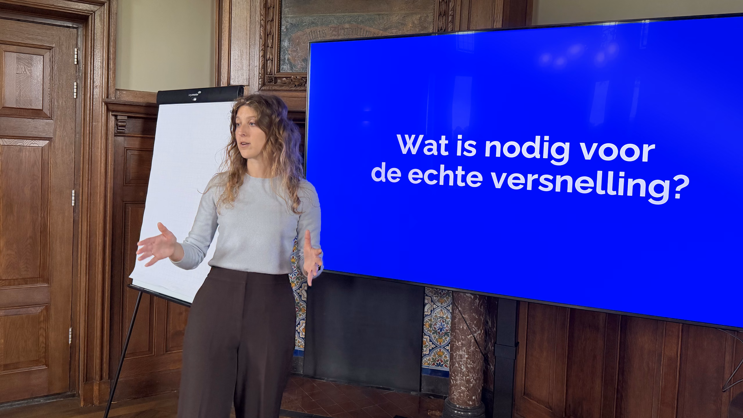 Lynn van Norden, partner van Factor10, geeft een presentatie bij een scherm met de vraag 'Wat is nodig voor de echte versnelling?'