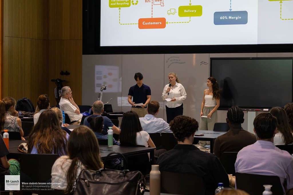 Drie studenten presenteren het verdienmodel van hun concept, met de vakjury en medestudenten in de zaal.